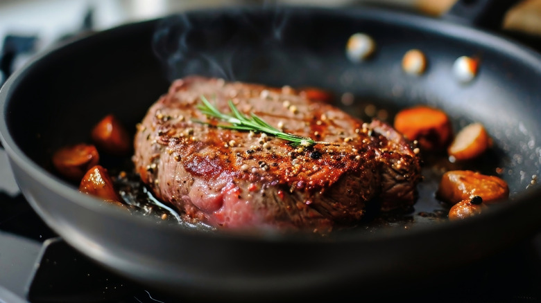 Seared steak cooking in pan with fresh herbs