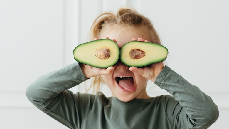 child holding avocados over eyes