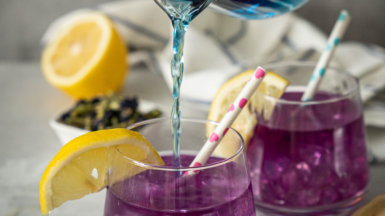 pouring blue liquid into purple cocktails