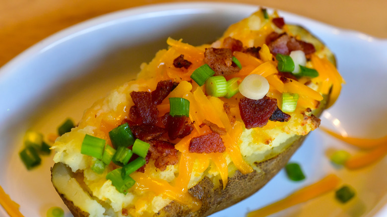 twice baked potato with melted cheddar, chives, and bacon on a white plate