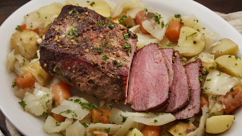 A plate of sliced corned beef surrounded by chunks of potatoes, carrots and caabage