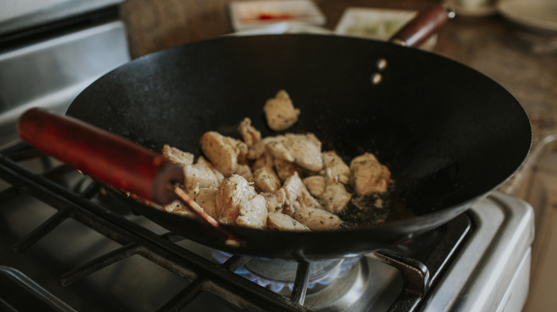 Chicken frying in a hot wok on gas range