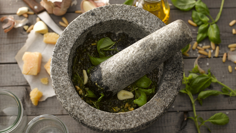 Mortar and pestle with pesto ingredients on wood tablde