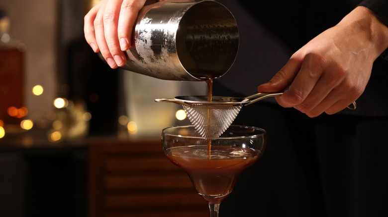 Hand pouring espresso martini through strainer