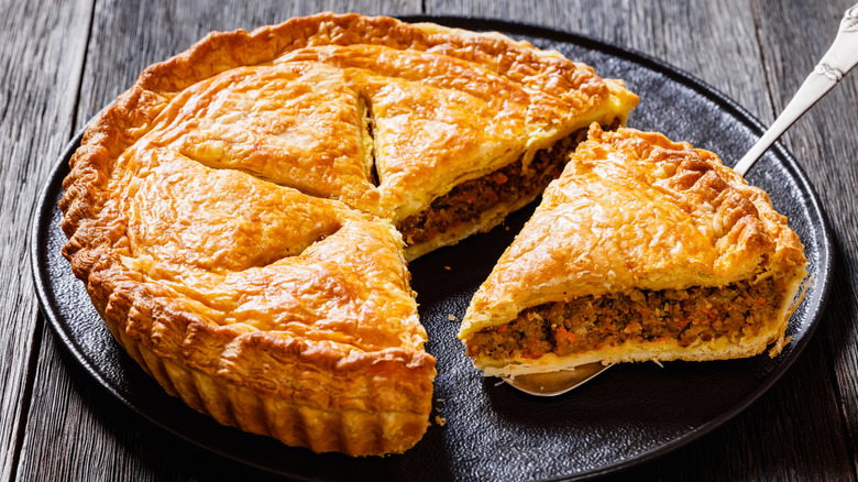 spatula lifting slice of meat pie with puff pastry shell