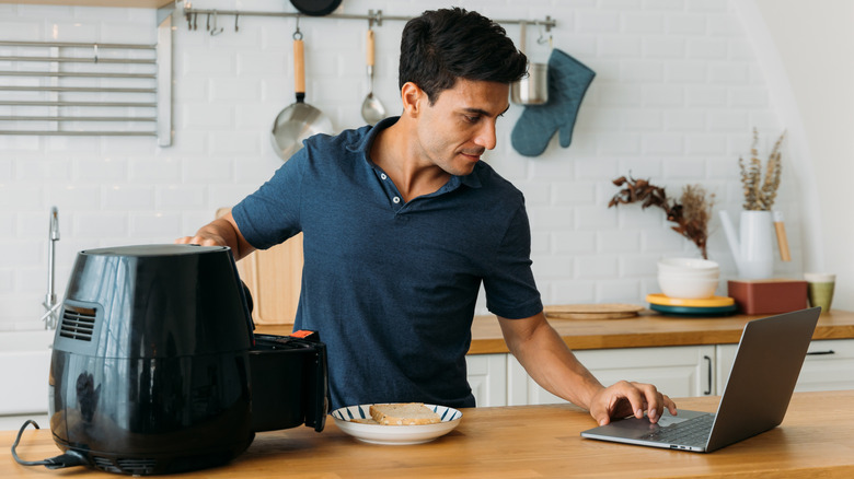 man using air fryer while referencing computer.