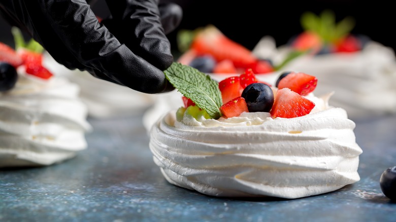 gloved fingers garnishing pavlova dessert