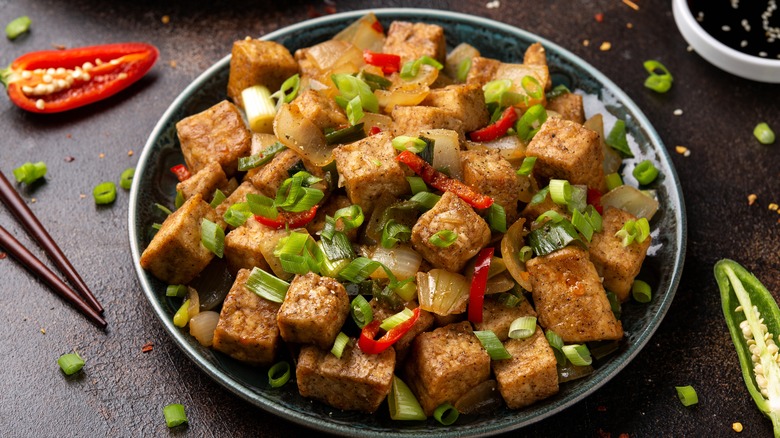 Bowl of black pepper tofu surrounded by scallions and chiles.