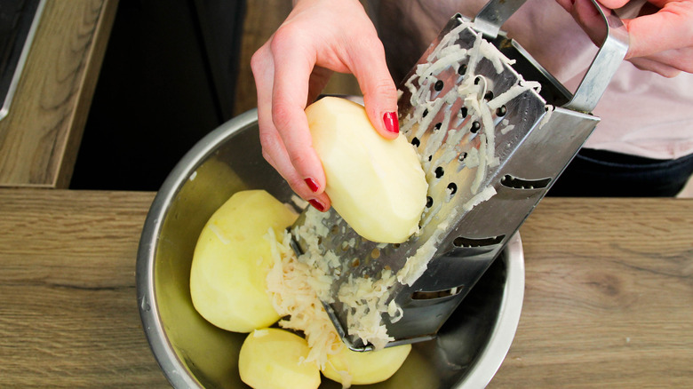 A person grating potatoes on a cheese grater into a bowl