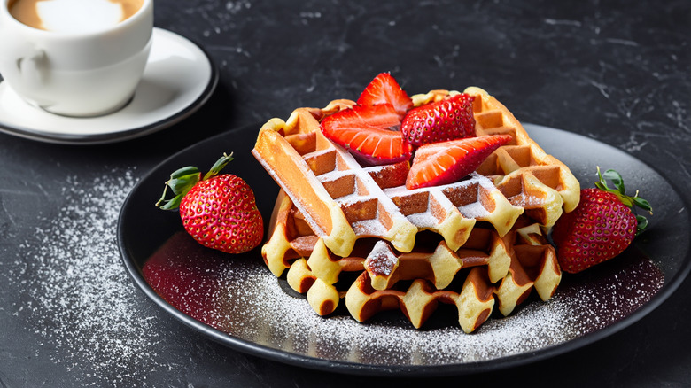 plate of waffles with powdered sugar and fresh strawberries