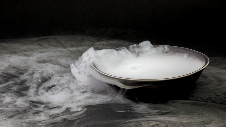 A bowl of dry ice steaming out all over black counter