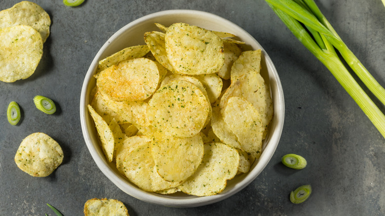 A bowl of sour cream and onion chips surrounded by fresh green onion.