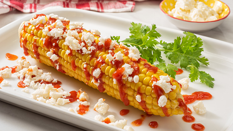 Grilled corn on the cob with hot sauce drizzle and cheese crumbles on top