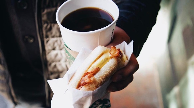 man holding coffee and breakfast sandwich