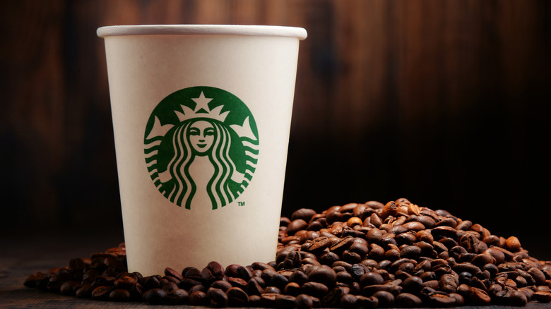 A Starbucks coffee cup surrounded by fresh coffee beans.