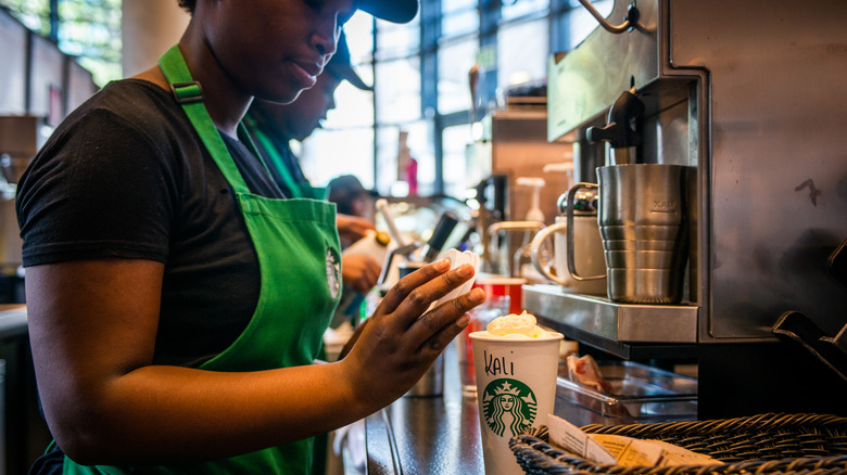 A Starbucks barista preparing a hot drink with whipped cream