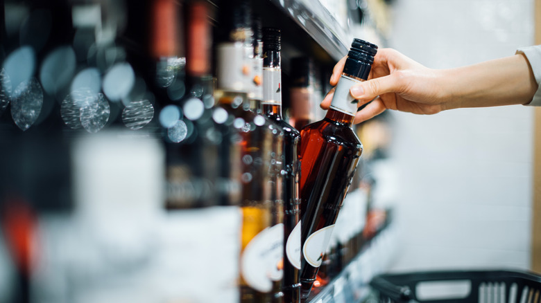 Hand taking liquor bottle off shelf