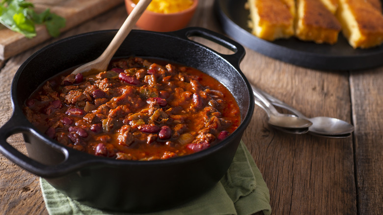 A cast iron pot of chili with a wooden spoon in it on a table