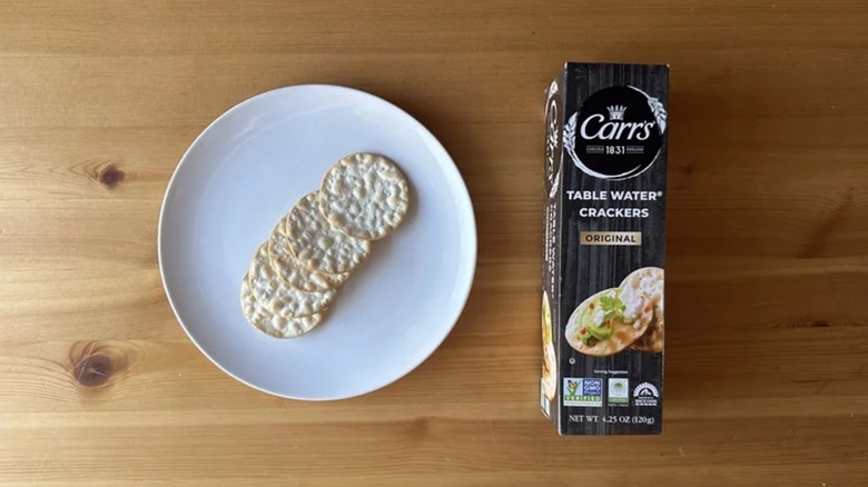 a few Carr's crackers spread out on a plate next to their box