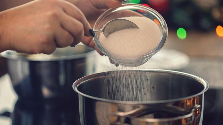 Woman's hands spooning granulated sugar into pot