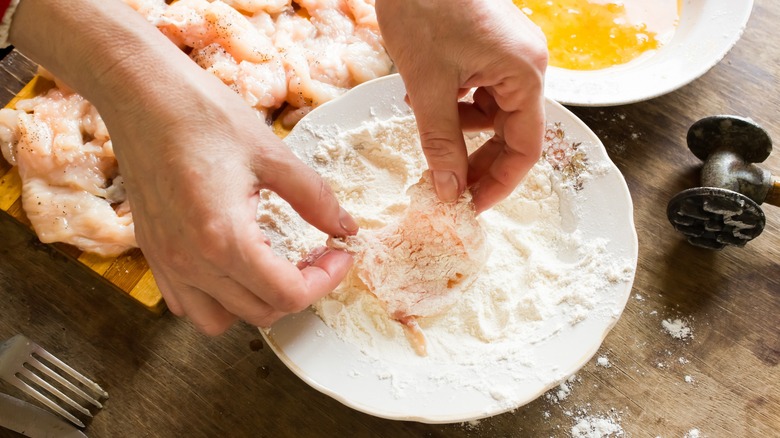 Hand dredging chicken in flour