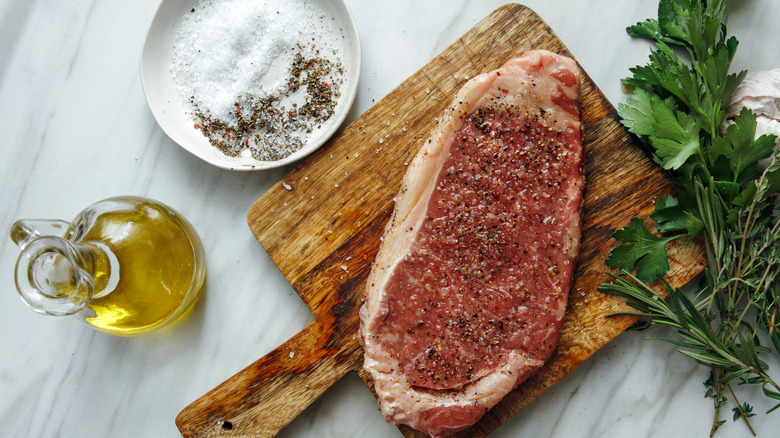 Raw steak on cutting board with seasonings and olive oil