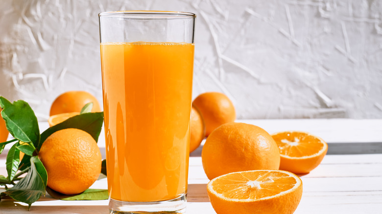 orange juice in glass next to halved oranges