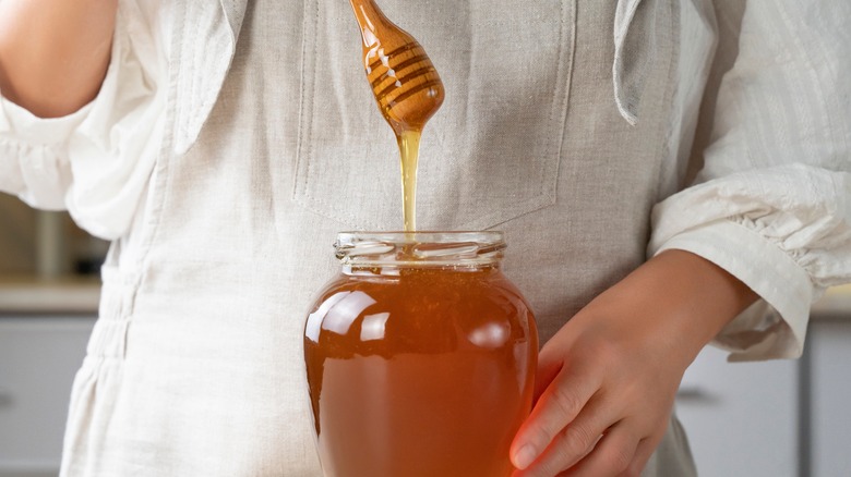 chefs hands holding a honey dipper over a glass jar of honey