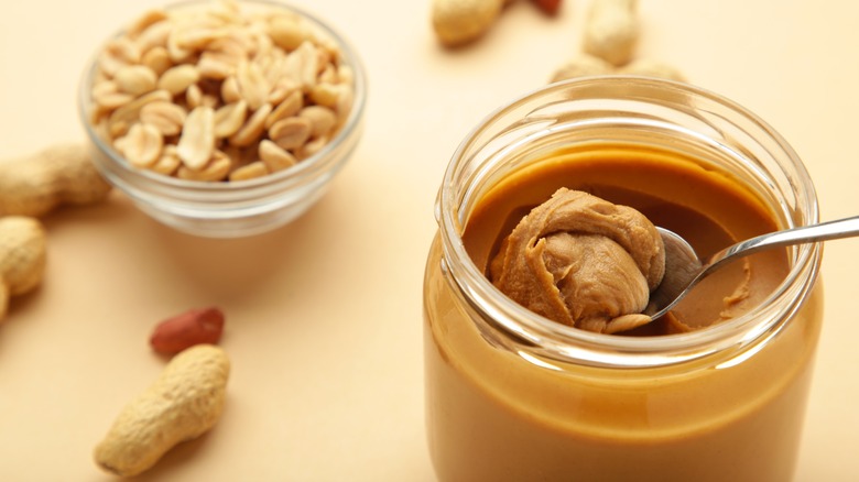 Jar of smooth peanut butter beside a dish of roasted peanuts