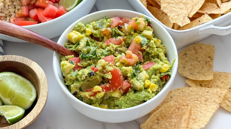 A bowl of guacamole with corn and tomatoes