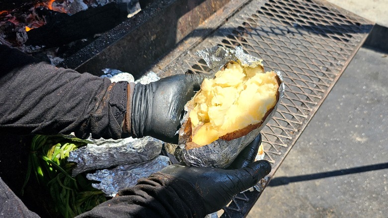 Hands holding a foil-wrapped potato