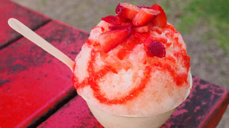 A cup of shaved ice top with red syrup and strawberries