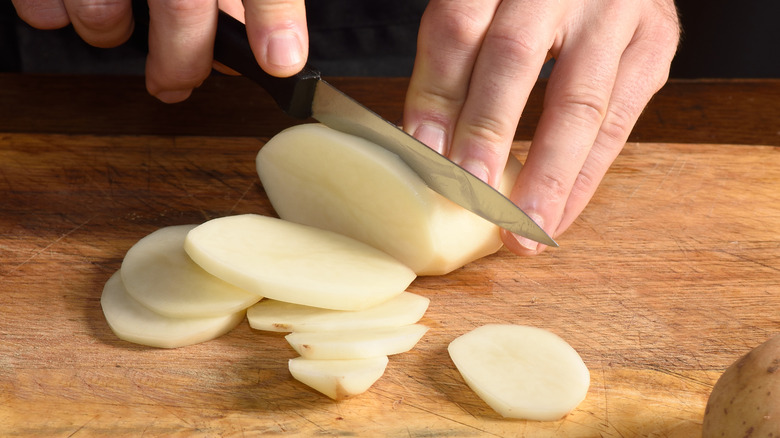 Hands slicing a potato with a paring knife
