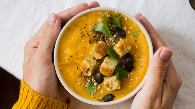 warming hands on pumpkin soup bowl