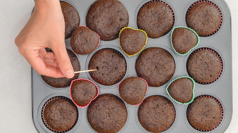 Someone tests a tray of chocolate cupcakes with a toothpick