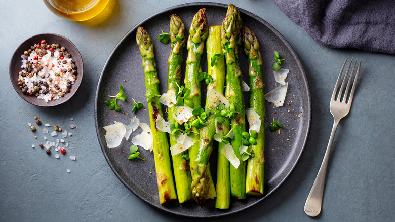 Roasted asparagus on plate beside a fork, salt, pepper, and a drink