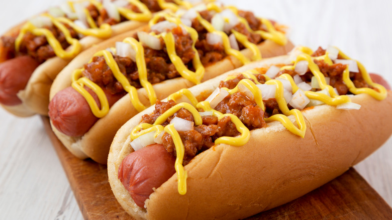 Three hot dogs topped with chili, mustard, and onions