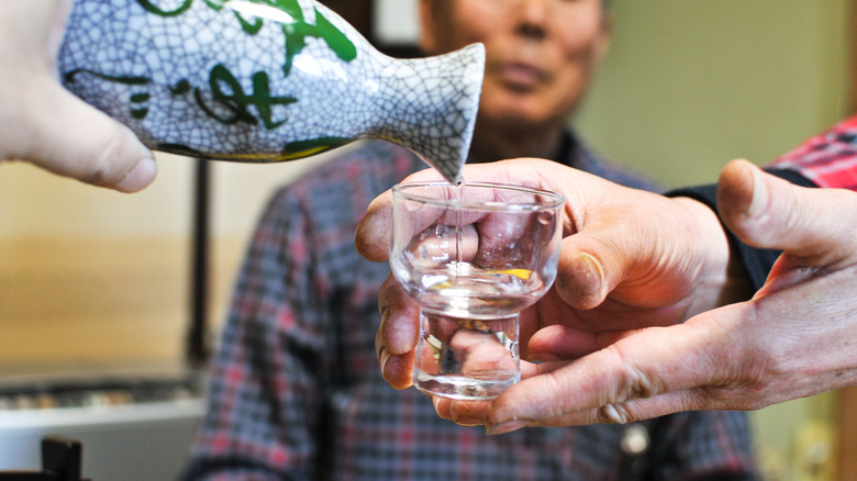 Hands pouring sake into a cup being held