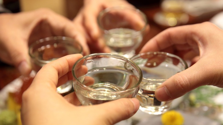 Four hands holding sake shots