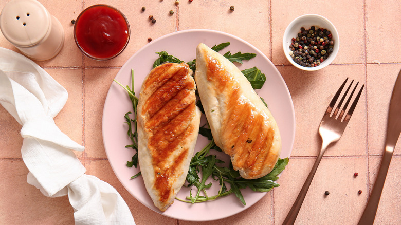 Two grilled chicken breasts on a pink plate