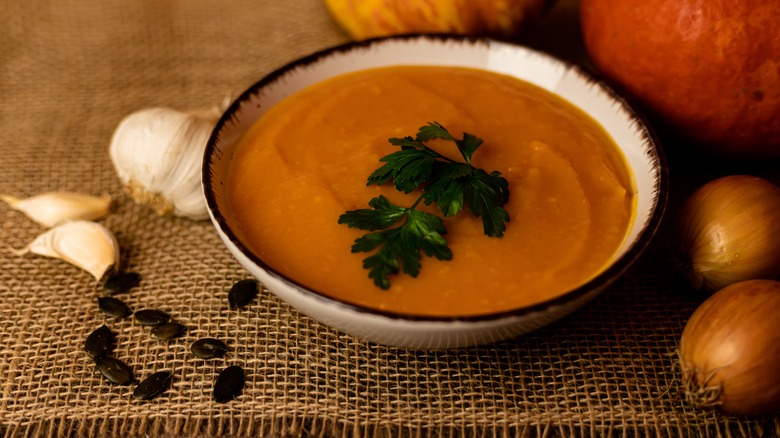 pumpkin soup in bowl with garlic and onions nearby