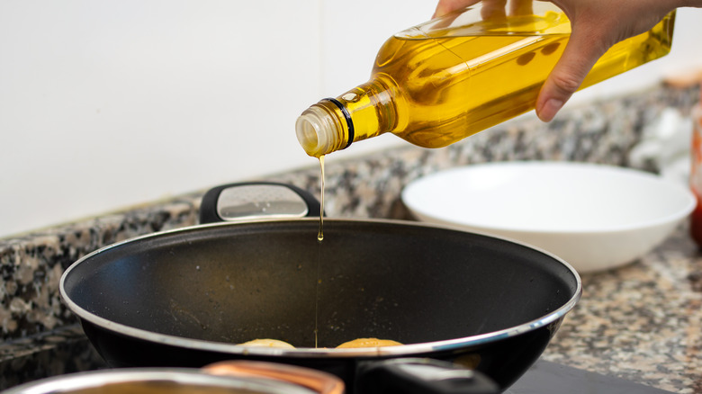 Hand pouring olive oil into pan