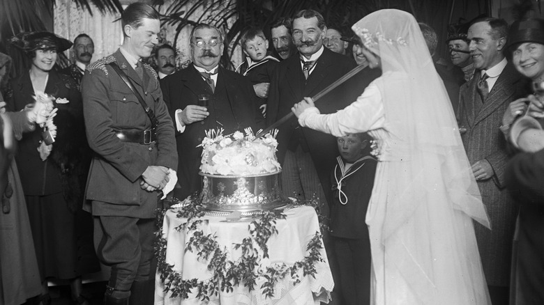 Bride cutting wedding cake with sword in 1918