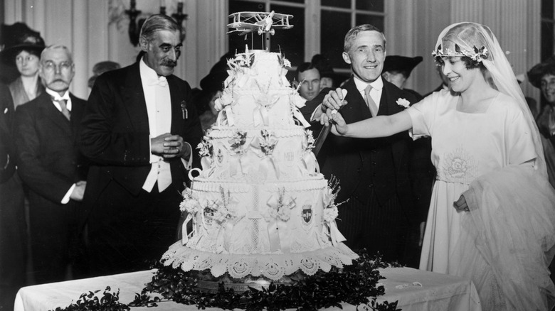 Couple cutting wedding cake in 1920 surrounded by guests