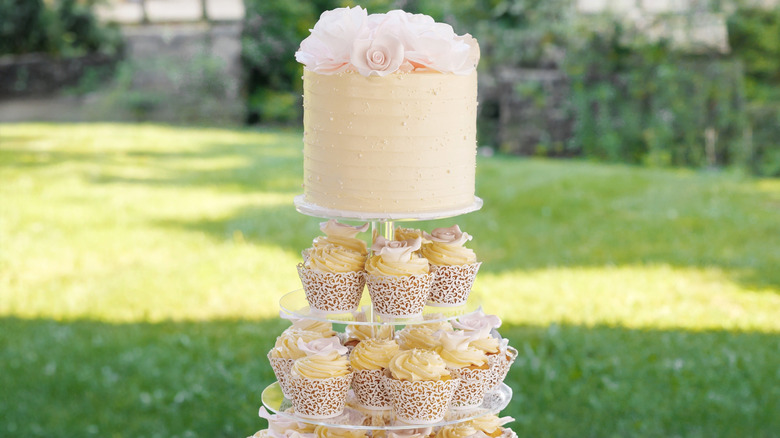 Wedding cake with tiers of cupcakes underneath outdoors