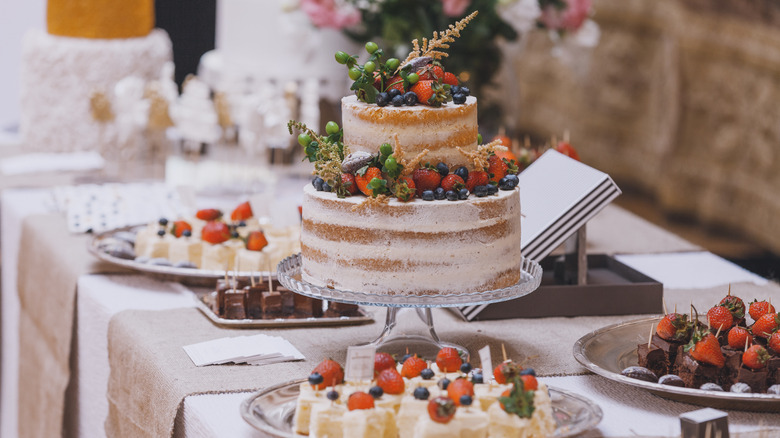 Naked wedding cake surrounded by other desserts