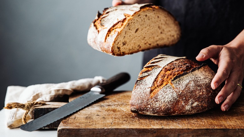 Hands slicing a loaf of sourdough bread