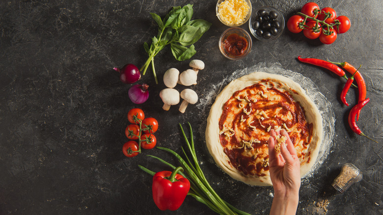 A wooden spoon spreading sauce onto pizza dough