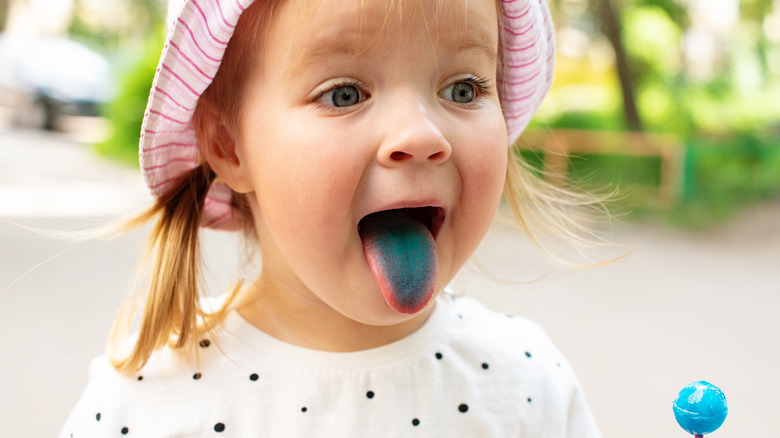 Little girl with blue lollipop and dyed tounge