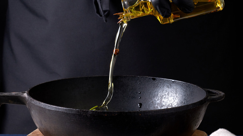 chef pouring infused oil into a cast iron pan on a black background